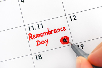 Woman fingers with pen writing reminder Remembrance Day in calendar.
