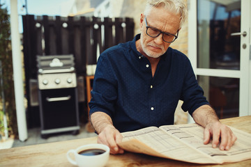 Senior man reading a newspaper outside on his patio