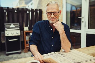 Smiling senior man relaxing on his patio with a newspaper