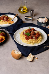 Homemade spaghetti or pasta with meatball and cheese in tomato sauce  placed in a white dish. On dark blue tablecloth on the table Along with a bottle of olive oil placed beside them.