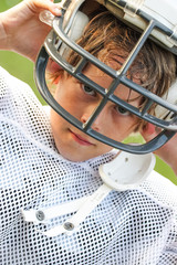 Young boy in a football uniform taking off his helmet after a game