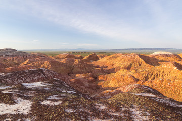 Multicolored red, orange and yellow striped hills with fragments of saline soil under a bright blue sky in Eastern Kazakhstan