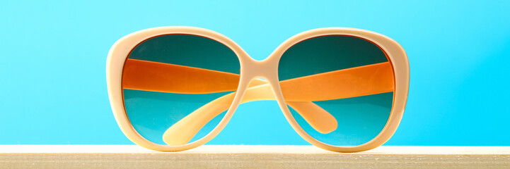 Fototapeta premium Yellow sunglasses on a wooden shelf on a blue pastel background. Minimalism.