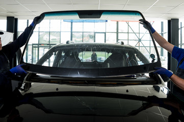 Automobile special workers remove old windscreen or windshield of a car in auto service station garage.