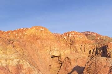 Small ravine in multicolored red, orange and yellow striped hills under a bright blue sky in...