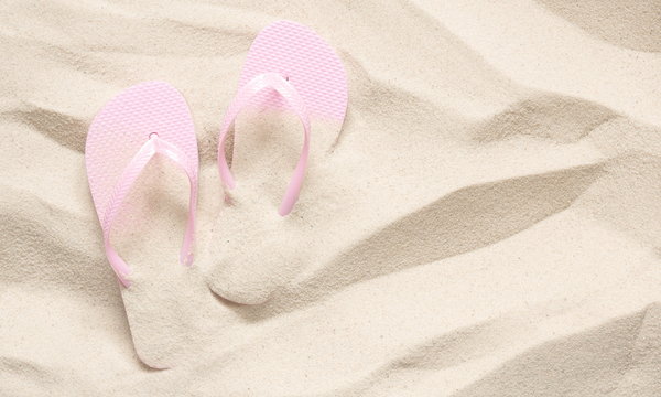 Beach pink flip-flops on a light sand. Texture of light sand. The concept of a beach holiday. Summer concept. Flat lay, top view, copy space 