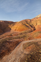 Creek bed in multicolored red, orange and yellow striped hills with saline soil under a bright blue sky in Eastern Kazakhstan, vertical