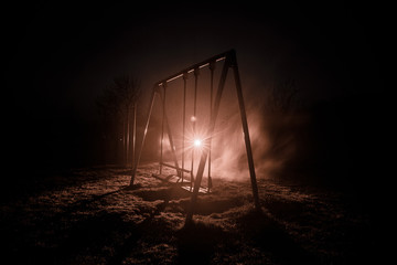 Night photo of metal swing standing outdoor at night time with fog and surreal toned light on...