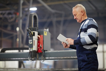 Serious mature worker with touchpad searching for online information while working in shipyard