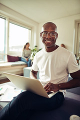 Fototapeta premium Smiling African businessman working on a laptop at his desk