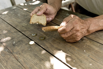 Hands the poor old man's, piece of bread and change, pennies on wood background. The concept of hunger or poverty. Selective focus. Poverty in retirement.Homeless.