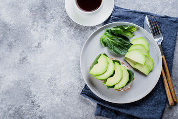 Healthy Vegetarian breakfast. Whole-grain toasts with cottage cheese, avocado, and spinach over grey concrete background, top view, copy space. Clean Eating, Gluten-free, Diet Food Concept