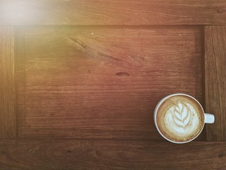 Latte coffee in white cup on old wooden table with light flare at corner show warm lighting.