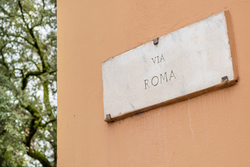 Old marble street sign Via Roma on a terracotta wall in Italy