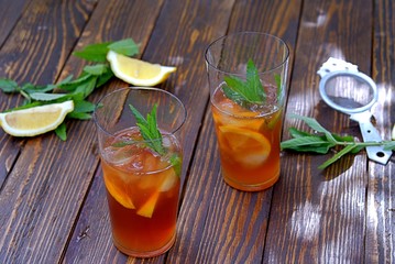 Cool drink, cold black tea with lemon, mint and ice in tall glasses. Summer concept