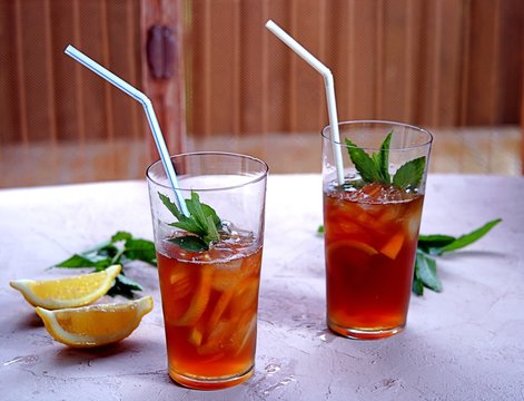 Cool drink, cold black tea with lemon, mint and ice in tall glasses on a concert background. Summer concept