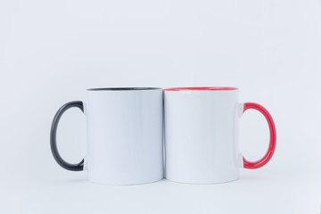 Two white mugs, with a black and red handle on a light background.