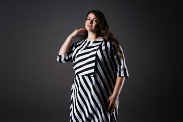 Plus size fashion model in striped dress, fat woman on gray background, overweight female body