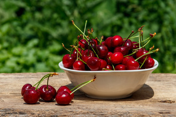 Bowl with fresh cherry on rustic wooden table outdoor