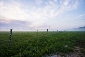 Colorful spring sunrise in Latvia. A view of the green country field under the morning fog