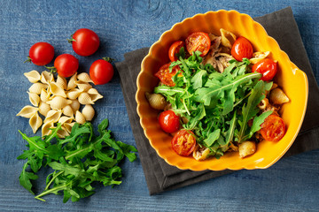Pasta with tuna and arugula in shaped plate on wooden background. top view