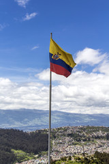 Flag of the Republic of Ecuador, on a sunny day with the city of Quito in the background.