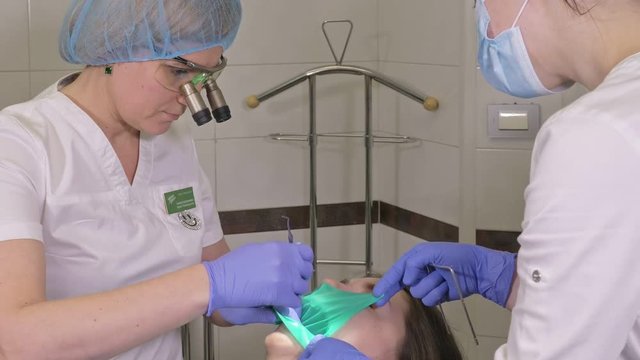 Woman at dentist clinic gets dental treatment to fill a cavity in a tooth. Dental restoration and composite material polymerization with UV light and laser. Installation of dental dam.