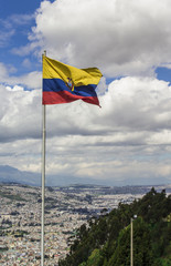 Flag of the Republic of Ecuador, on a sunny day with the city of Quito in the background.