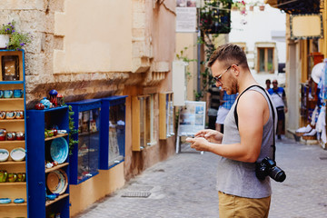 Traveller with camera on his shoulder navigates with smartphone through the narrow streets of the foreign city Chania, Crete, Greece