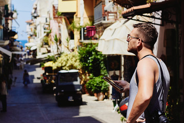 Traveller with camera on his shoulder navigates with smartphone through the narrow streets of the foreign city Chania, Crete, Greece