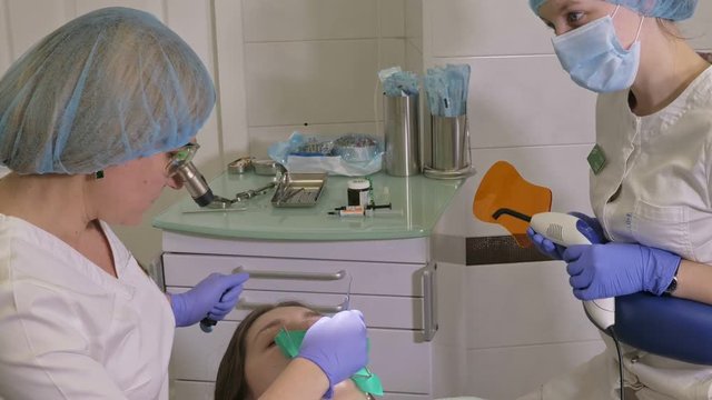 Woman at dentist clinic gets dental treatment to fill a cavity in a tooth. Dental restoration and composite material polymerization with UV light and laser. The doctor works with an assistant.