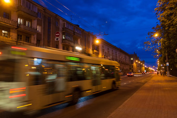The motion of a blurred trolleybus in the street in the evening.