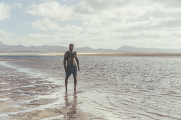 Handsome muscular bearded man standing on the sea shore at sunrise. Side portrait of healthy young bearded man running at the beach with bright sunlight.