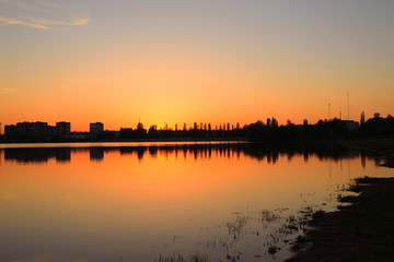 Fototapeta na wymiar Warm summer sunset over the city lake and beach. Evening cityscape.