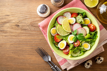 Fresh salad with vegetables and quail eggs on rustic wooden background