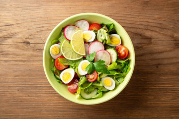 Fresh salad with vegetables and quail eggs on rustic wooden background