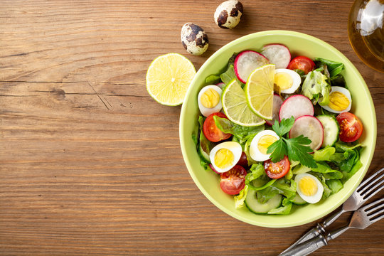 Fresh salad with vegetables and quail eggs on rustic wooden background