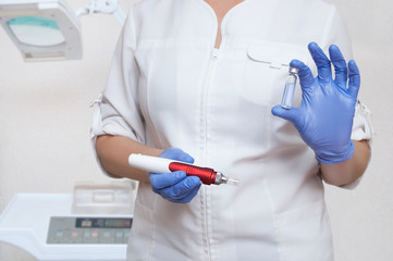 The cosmetologist in sterile gloves holds an electric appliance for mesotherapy of the facial skin...