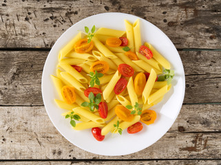 Penne pasta with tomatoes decorated with basil on old rustic gray wooden background, low-calorie diet, top view
