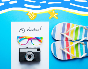 photo of sheet of paper My Vacation, colorful sandals, glasses and retro camera on the wonderful blue studio background