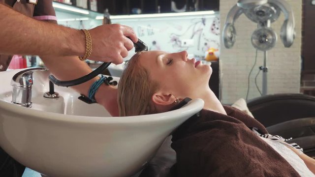 Male stylist washing a blond woman's head in a modern beauty salon
