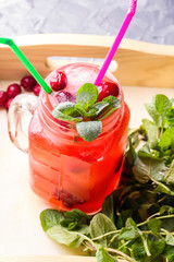 Berry Morse, cocktail of currant and cowberry with ice and fresh mint leaves, with powdered sugar in cocktail drinking jars with colored drinking straws in a wooden box