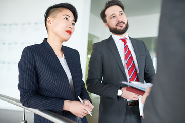 Attractive Asian entrepreneur with stylish haircut listening to her business partner with concentration while discussing mutually beneficial cooperation at office lobby