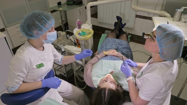 Woman at dentist clinic gets dental treatment to fill a cavity in a tooth. Dental restoration and composite material polymerization with UV light and laser. The doctor works with an assistant.