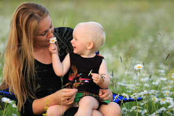 Mała dziewczynka bawi się z matką kwiatkami na łące. - obrazy, fototapety, plakaty