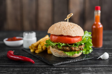 Tasty hamburger with meat and vegetables against a dark background. Fast food. It can be used as a background