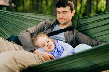 Obraz premium Happy people outdoor. Lifestyle family. Father with his litle artistic funny little child girl resting and playing at nature. Adult male parent with young beautiful daughter lying in hammock in summer