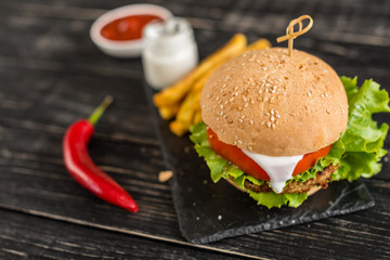 Tasty hamburger with meat and vegetables against a dark background. Fast food. It can be used as a background