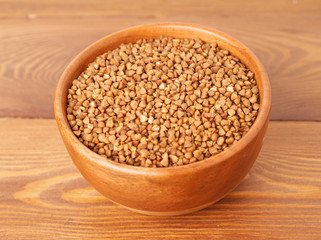 Dry buckwheat in wooden bowl on brown wooden background. Side view.
