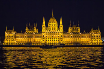 Fototapeta premium View on Danube river and the illuminated building of Parliament from viewpoint on a touristic motor ship at night in Budapest, Hungary